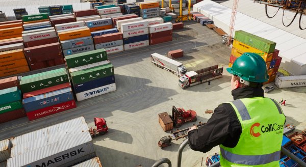 Employee wearing security helmet and branded vest, looking down at the containers ready to be shipped by sea