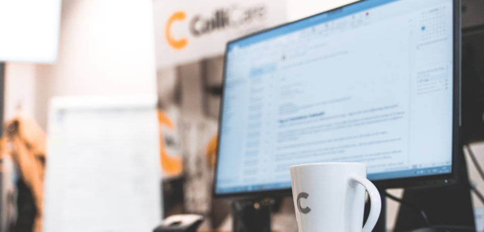 A computer at a desk surrounded by branded ColliCare mug and banner